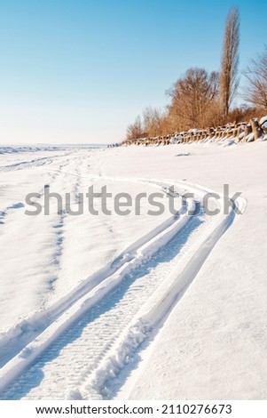 The trail of a snowmobile on a frozen river in snowy winter