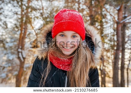 Portrait of a charming little girl in a red hat in a snowy forest in winter. Christmas winter holidays. Happy childhood