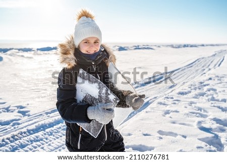 A happy little girl carries large transparent pieces of ice from the river on a frosty winter day