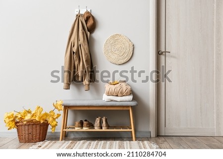 Jacket and hat hanging on light wall and basket with autumn leaves in interior of stylish hallway Royalty-Free Stock Photo #2110284704