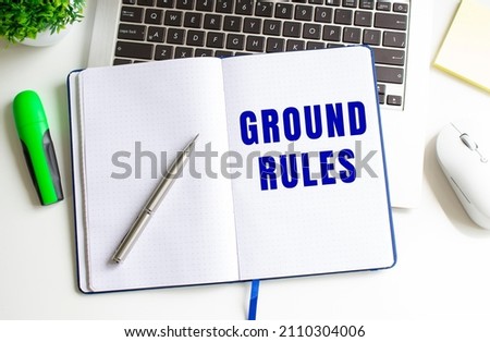 Modern white office desk with laptop and other accessories. Creative flat lay photo of workspace desk. Notepad with the text GROUND RULES in the middle. View from above.