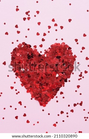 Valentine's day background. Heart made of shiny red small decorative hearts on a pink background. Flat lay, place for text. Festive minimal composition. Vertical image.