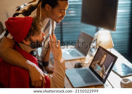 Stylish gay couple having video call with female colleague while sitting at cozy home office. Concept of online meetings and remote work from home. Idea of homosexual relations while work