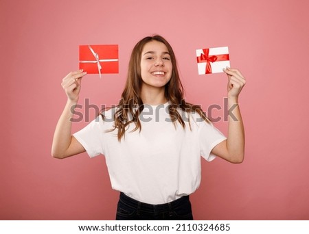 Happy smiley young teenager girl in white t-shirt hold two different gift certificates isolated on pink background. People lifestyle concept.