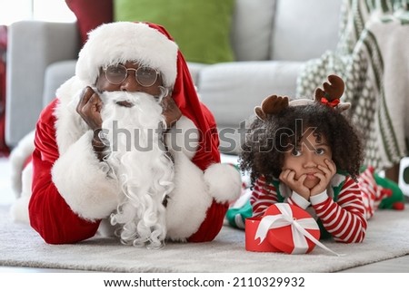 Little African-American girl with Christmas gift and Santa Claus at home