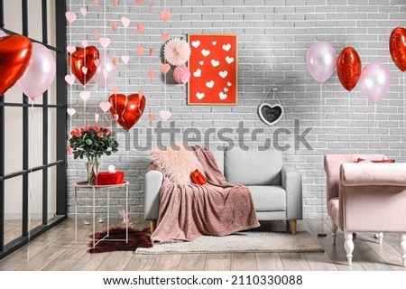 Interior of room decorated for Valentine's day with air balloons and comfortable sofas near grey brick wall Royalty-Free Stock Photo #2110330088