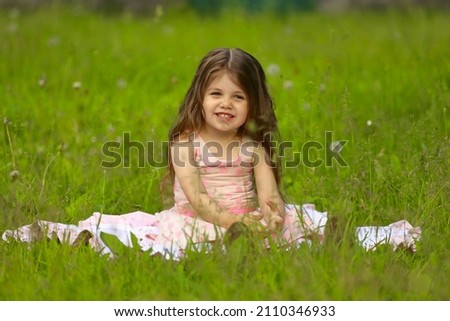 a little girl with long hair sits on the grass in the park in the summer. High quality photo