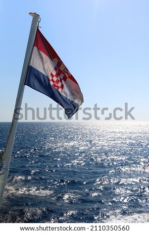 Flag of Croatia blowing in the wind. Adriatic sea, island and boats in the background.