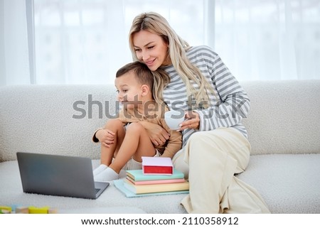 adorable cute kid boy watching cartoons, spending time with mom at home. caucasian european friendly family have rest together, enjoy holidays weekends, in bright living room, using laptop