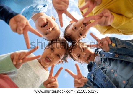 childhood, leisure and people concept - multiethnic group of happy children showing peace gesture under blue sky