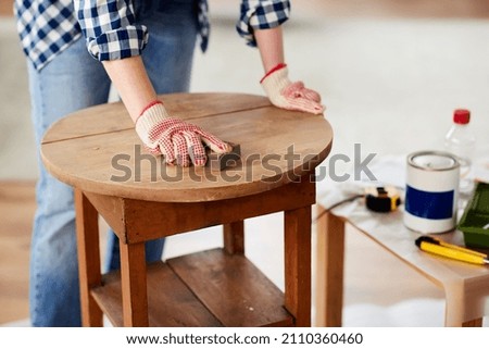 furniture renovation, diy and home improvement concept - close up of woman sanding old wooden table with sponge Royalty-Free Stock Photo #2110360460