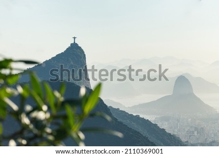 Two mountains in the distance at sunrise with foliage in foreground and statue silhouette