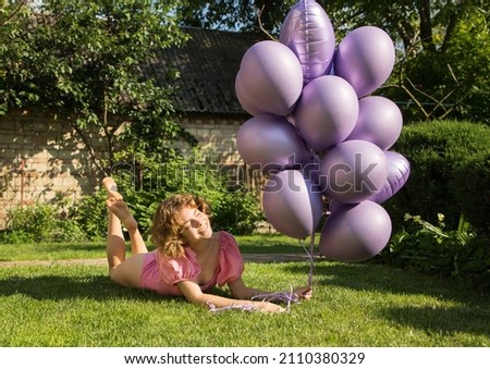 happy beautiful tender girl 17-18 years old with bunch of purple helium balloons lies on green lawn. Birthday girl. Happy day. concept of joy, positivity and congratulations. Dreams, festive mood