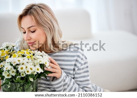 Carefree stylish good-looking woman ordered flowers for home, close eyes smiling and sniffing beautiful bouquet of wildflowers, sitting satisfied in bright cozy living room. portrait Royalty-Free Stock Photo #2110386152