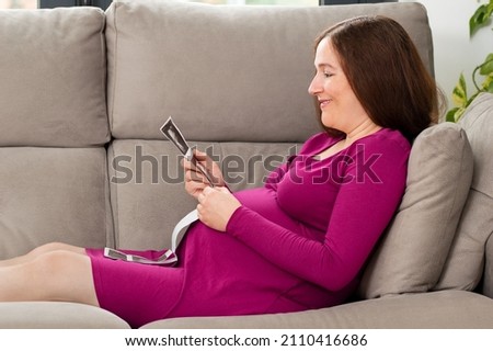 Shot of a pregnant woman looking at a sonogram picture at home