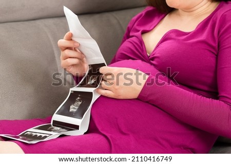 Shot of a pregnant woman looking at a sonogram picture at home