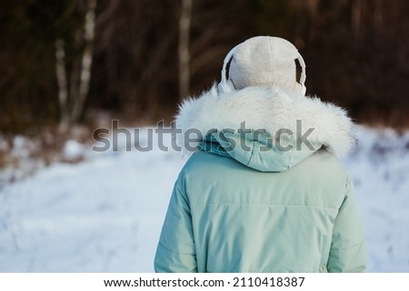 Photo of lonely young girl with headphones in winter park in dreams and complete calm standing with her back to the camera