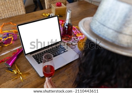 Cropped image of biracial young woman with champagne enjoying party on video call, copy space. unaltered, wireless technology, video call and distant party celebration.