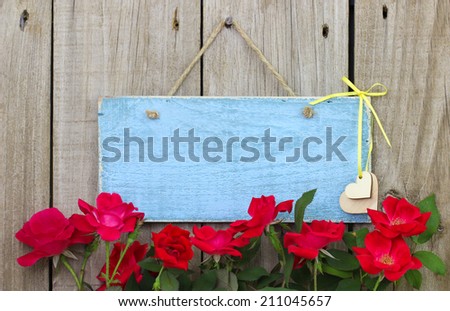 Flower border of red roses by antique blue blank sign with hearts hanging on fence