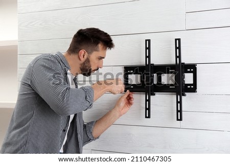 Man with screwdriver installing TV bracket on wall indoors Royalty-Free Stock Photo #2110467305