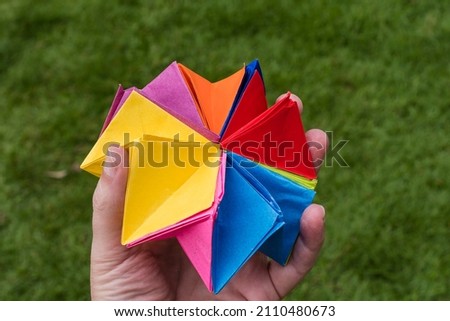Origami. Hand holding colorful paper folding over garden grass.
