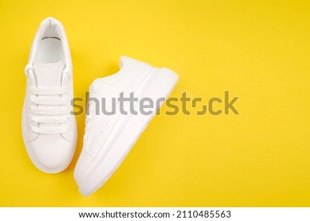 A pair of stylish women's leather shoes on a high platform with laces on a yellow background.Casual comfortable white shoes.Seasonal sales, discounts on shoes. Proper care for white skin.Copyspace Royalty-Free Stock Photo #2110485563