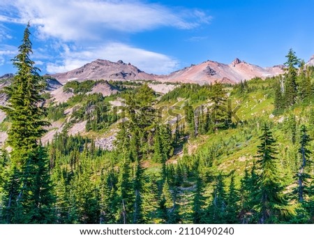 Old volcanic terrain rises above an alpline meadow at Goat Rocks Wilderness Area in Washington State. Royalty-Free Stock Photo #2110490240