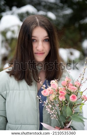Beauty teen age girl with brunette hair holding gentle pink roses outside on snow day in early spring