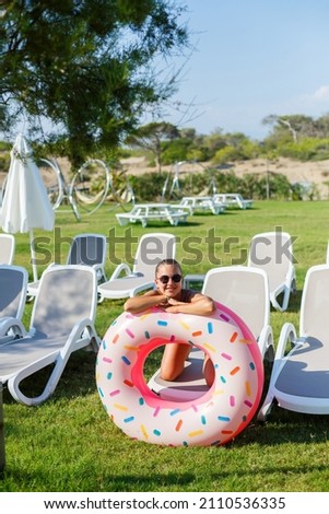 A young woman in a stylish swimsuit and sunglasses holds an inflatable donut ring in her hand. Beautiful happy girl posing and having fun in the sun. Vacation. travel