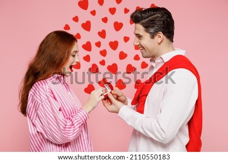 Young side view couple two friends woman man 20s in casual shirt make a proposal give engagement ring isolated on plain pastel pink background studio. Valentine's Day birthday holiday party concept.