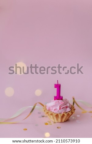 a beautiful picture of a cupcake with pink butter cream and cherry with a number 1 one candle on the top of it isolated on pink background. Festive Happy first birthday mood. Card design idea. 