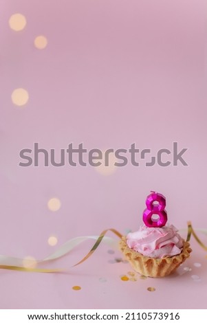 a beautiful picture of a cupcake with pink butter cream and cherry with a number 8 candle on the top of it isolated on pink background. Festive Happy birthday mood. Card design idea. 