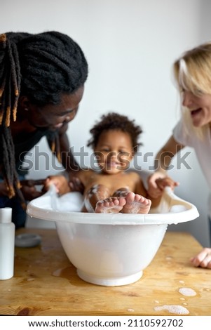 cheerful laughing Infant black baby toddler taking bath with foam bubbles. Parents Bathing and washing little kid with dark skin. Children care and hygiene concept. focus on feet of child