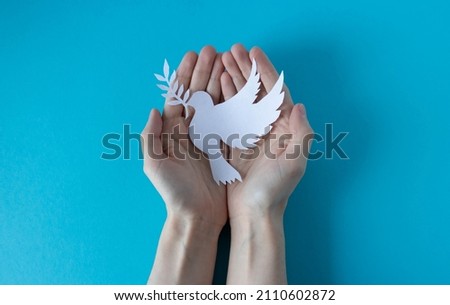 Hands holding a paper white pigeon on a blue background. World Peace Day. World Science Day for Peace and Development Royalty-Free Stock Photo #2110602872
