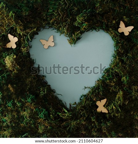 Amazing theme that inspires spring and love, a background of green moss with open sky in the shape of a heart and butterflies that announce the awakening of nature on the light blue background Royalty-Free Stock Photo #2110604627