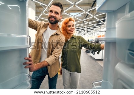 Young couple choosing a refrigerator in a home appliances and electronics store. Inside view. Buying a new refrigerator.