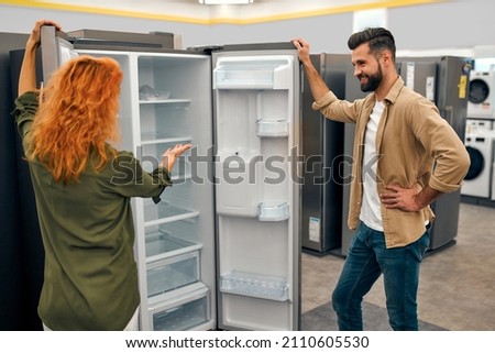 A young couple is choosing a new refrigerator in a home appliances and electronics store. Buying a new refrigerator.