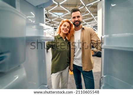 Young couple choosing a refrigerator in a home appliances and electronics store. Inside view. Buying a new refrigerator.