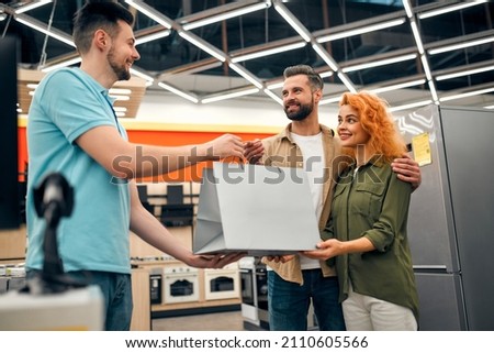 A young couple at the checkout picking up a purchase from a salesperson in a home appliances and electronics store. Royalty-Free Stock Photo #2110605566