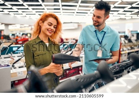 A beautiful red-haired girl is talking to a male salesperson while getting help buying a new hair dryer at a home appliances and electronics store. Royalty-Free Stock Photo #2110605599