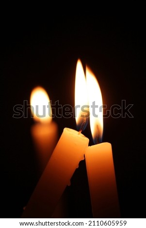 
Close-up picture of two lit candles touching each other against a black background