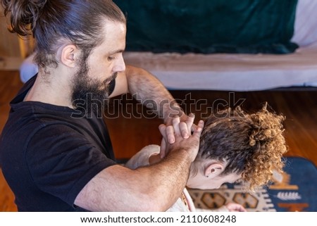 A professional masseur, is seen from the side with clasped hands applying pressure to the head and neck of female client with copy space in top right.