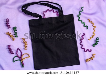 Mardi Gras Mockup black tote bag with glitter decor on fabric lilac background, flat lay, top view, copy space.