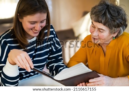 Grandmother and her young granddaughter spent great time together, family members look at photos from the youth of an elderly parent, through the pages of the album and recall funny stories from life. Royalty-Free Stock Photo #2110617155
