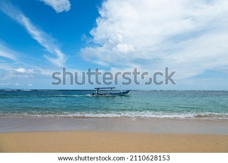 Traditional fishing boats called jukung on the white sand beach. Nusa dua beach, Bali island, Indonesia. High waves with foam spread on the coast. Amazing blue sky with clouds.