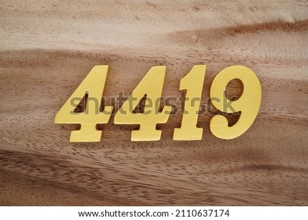Wooden Arabic numerals 4419 painted in gold on a dark brown and white patterned plank background.