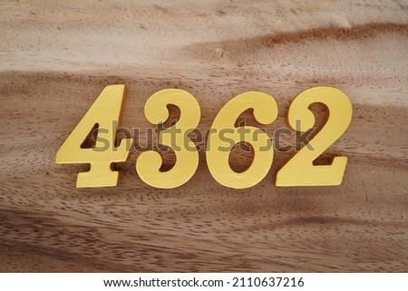 Wooden Arabic numerals 4362 painted in gold on a dark brown and white patterned plank background.