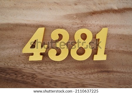 Wooden Arabic numerals 4381 painted in gold on a dark brown and white patterned plank background.
