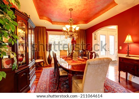 Luxury dining room with rich dining table. Bright red walls blend perfectly with designed ceiling