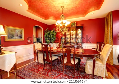 Luxury dining room with rich dining table. Bright red walls blend perfectly with designed ceiling